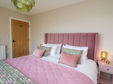 A bedroom with a pink upholstered bed headboard a pink quilt and floral pillows next to a wooden door at Dol Blodau in Newbridge-On-Wye