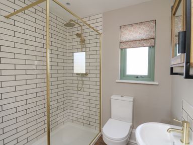 A bathroom with a shower area a toilet a window with a patterned blind and a sink at Dol Blodau in Newbridge-On-Wye