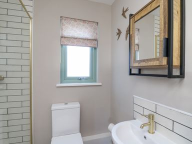 A bathroom with a toilet sink wooden framed mirror and window with patterned blind at Dol Blodau in Newbridge-On-Wye