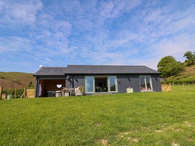 A single story house with patio furniture on a grassy hill at Dol Blodau in Newbridge-On-Wye