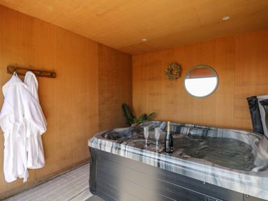 A hot tub with two glasses and a bottle inside a wooden room with two robes hanging on hooks at Dol Blodau in Newbridge-On-Wye