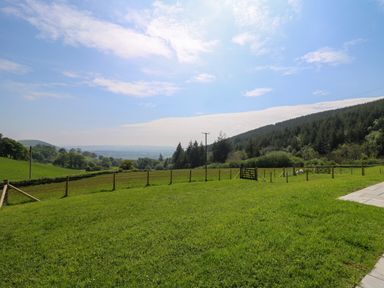A fenced grassy field with trees hills and a partly cloudy sky at Dol Blodau in Newbridge-On-Wye