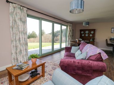 A living room with a purple sofa, wooden coffee table, floral curtains, and large glass sliding doors at Ystrad Wen in Llysdinam near Newbridge-On-Wye
