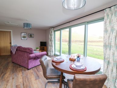 A dining table set for two next to large glass doors with a purple sofa and wooden floor in the living room at Ystrad Wen in Llysdinam near Newbridge-On-Wye