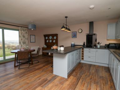 A kitchen with an island, dining table with chairs, wooden floor and glass doors showing a view at Ystrad Wen in Llysdinam near Newbridge-On-Wye