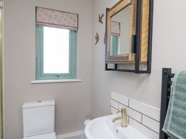 A bathroom with a toilet, window with patterned blind, wall-mounted mirror, sink with gold faucet, and towel on rack at Ystrad Wen in Llysdinam near Newbridge-On-Wye