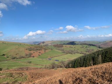 A rural landscape with hills fields trees and two houses under a blue sky at Ystrad Wen in Llysdinam near Newbridge-On-Wye