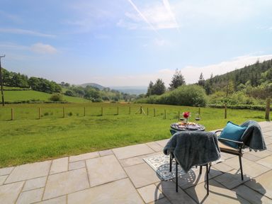 A patio with two chairs and a table set with wine and snacks overlooking a fenced grassy field at Ystrad Wen in Llysdinam near Newbridge-On-Wye