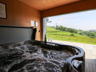 An indoor hot tub with bubbling water next to an open large window showing green fields and trees at Ystrad Wen in Llysdinam near Newbridge-On-Wye