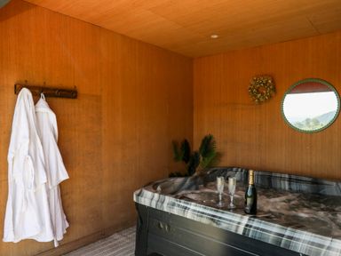 A room with a hot tub filled with water two white robes hanging on hooks a round mirror and a wreath on a wall at Ystrad Wen in Llysdinam near Newbridge-On-Wye