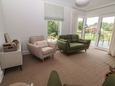 A sitting room with a beige armchair and a green loveseat near glass doors overlooking a garden at Shannon Vale in Woodford County Galway