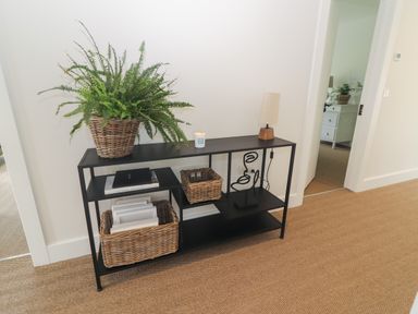 A hallway with a black metal shelf holding wicker baskets, books, a lamp, a candle, and a potted fern at Shannon Vale in Woodford County Galway
