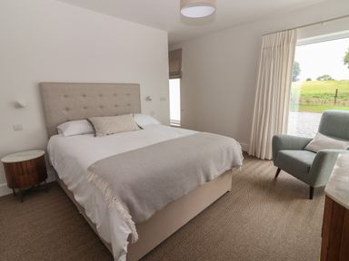 A bedroom with a bed side table and armchair near a window at Shannon Vale in Woodford County Galway
