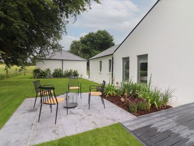 An outdoor patio with four chairs and a small table next to a white house with garden plants at Shannon Vale in Woodford County Galway
