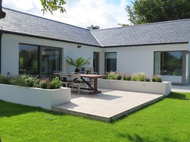 An outdoor patio area with a wooden dining table and metal chairs surrounded by raised planters and grass at Shannon Vale in Woodford County Galway