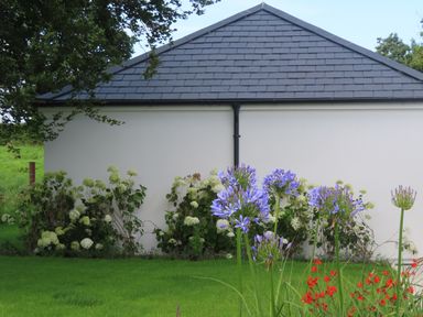 A white building with a slate roof and flowers in front at Shannon Vale in Woodford County Galway