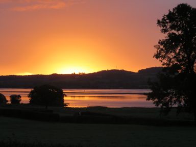 A sunset over a body of water with hills in the background and trees in the foreground at Shannon Vale in Woodford County Galway