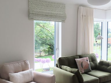 A living room with a beige armchair and a green sofa next to large windows with patterned and plain curtains at Shannon Vale in Woodford County Galway