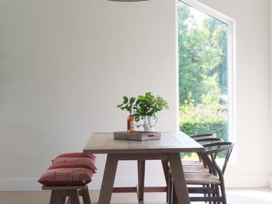 A dining table with two chairs on one side and a bench with three red cushions on the other side with a tray holding a bottle, two glasses, and a jug with greenery next to a large window showing trees outside at Shannon Vale in Woodford County Galway