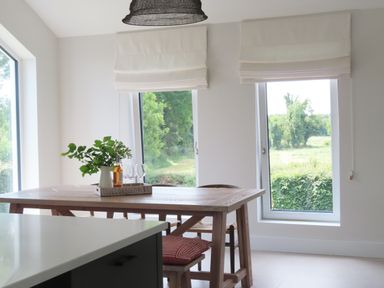 A dining area with a wooden table and chairs near large windows overlooking greenery at Shannon Vale in Woodford County Galway