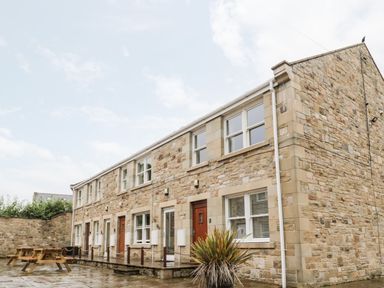 A stone building with multiple windows and doors beside a wooden picnic table at 2 Apple Tree in Beadnell