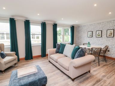 A living room with a beige sofa, armchair, ottoman, dining table, chairs, and green curtains at 2 Apple Tree in Beadnell
