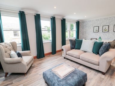 A living room with a beige sofa and armchair with teal curtains at 2 Apple Tree in Beadnell
