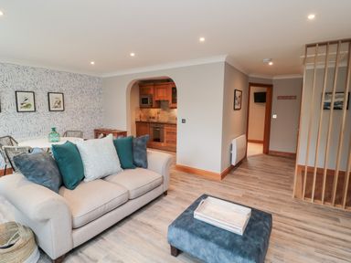 A living room with a sofa and ottoman adjacent to a dining area and kitchen at 2 Apple Tree in Beadnell