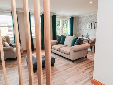 A living room with a beige sofa with cushions, armchair, ottoman, dining table with chairs and decorative items at 2 Apple Tree in Beadnell