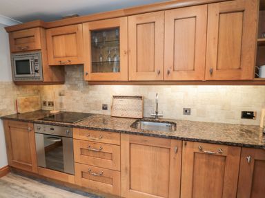A kitchen with wooden cabinets a granite countertop a stainless steel oven and microwave and a sink at 2 Apple Tree in Beadnell