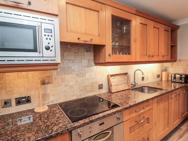 A kitchen countertop with stovetop oven microwave sink wooden cabinets and various kitchen items at 2 Apple Tree in Beadnell