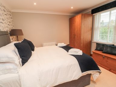 A bedroom with a bed with black pillows and white bedding two white towels two lamps a wooden wardrobe and a wooden chest under a window at 2 Apple Tree in Beadnell