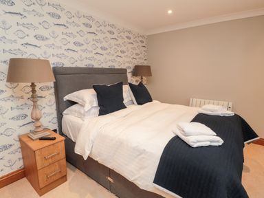 A bedroom with a bed with white bedding and black pillows and blankets beside wooden nightstands with lamps at 2 Apple Tree in Beadnell