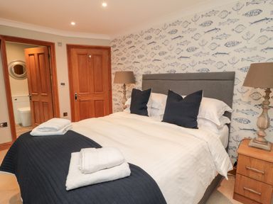 A bedroom with a bed with white and dark bedding two lamps and wooden doors at 2 Apple Tree in Beadnell