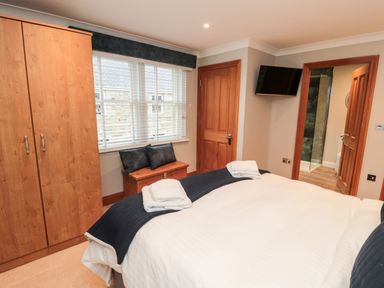 A bedroom with a bed towels on the bed wooden wardrobe window with blinds and a door leading to a bathroom at 2 Apple Tree in Beadnell