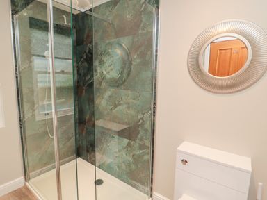 A bathroom with a glass enclosed shower with green stone walls a white toilet and a round wall mirror at 2 Apple Tree in Beadnell