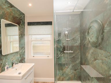 A bathroom with a sink and mirror next to a glass-enclosed shower with tiled walls at 2 Apple Tree in Beadnell