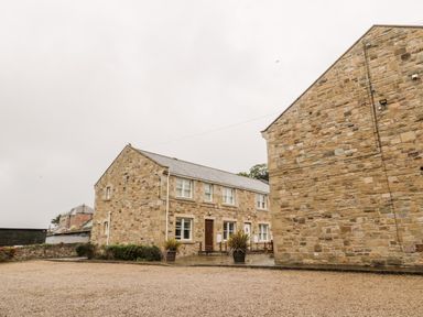 A gravel driveway with two stone buildings and potted plants at 2 Apple Tree in Beadnell