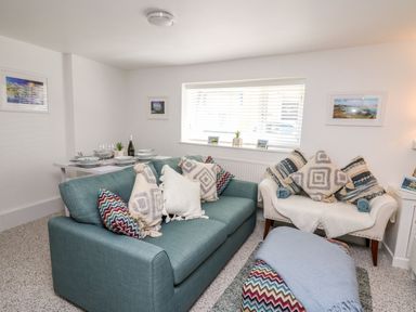 A living room with a teal sofa and white armchair with patterned cushions and a dining table at Lane Cottage in Cardigan