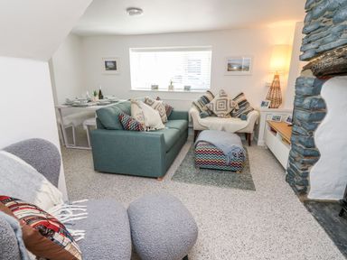 A living room with sofas cushions ottoman and a stone fireplace at Lane Cottage in Cardigan