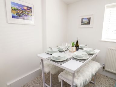 A dining area with a white table set for four with bowls forks wine glasses a bottle a small plant and two framed pictures on the walls at Lane Cottage in Cardigan