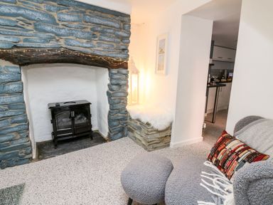A room with a stone fireplace and a black stove with a gray armchair and matching ottoman at Lane Cottage in Cardigan