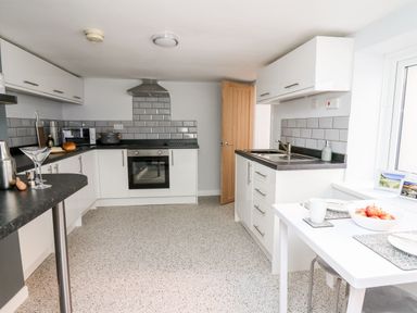 A kitchen with white cabinets a black countertop a stove a sink and a small dining table with apples at Lane Cottage in Cardigan
