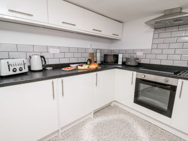 A kitchen with white cabinets black countertop toaster kettle microwave and oven at Lane Cottage in Cardigan