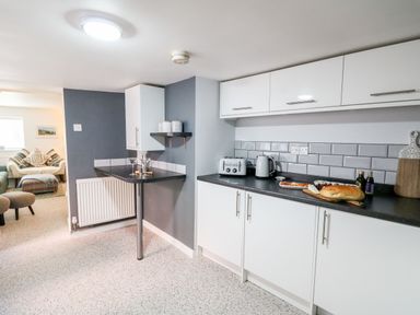 A kitchen with white cabinets countertop appliances and food with a view into a living room at Lane Cottage in Cardigan