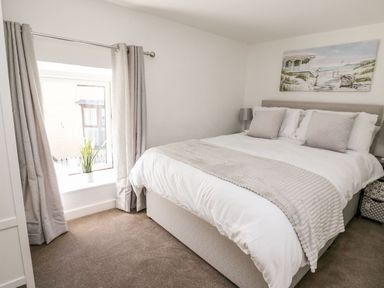 A bedroom with a bed curtains a window and a painting at Lane Cottage in Cardigan