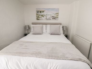 A bed with pillows and a blanket with two bedside tables and lamps a painting above the bed at Lane Cottage in Cardigan