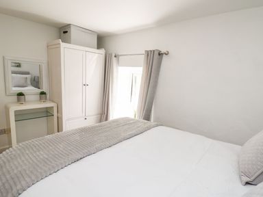A bedroom with a bed a white wardrobe a white table with two small plants a mirror and light gray curtains at Lane Cottage in Cardigan