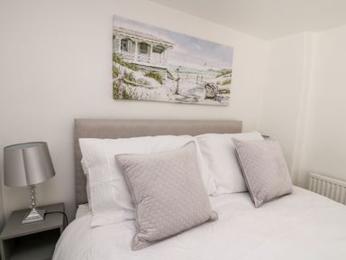 A bedroom with a bed two pillows a lamp on a bedside table and a beach painting on the wall at Lane Cottage in Cardigan