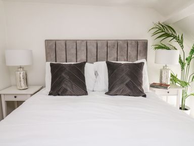 A bed with a gray headboard two dark gray pillows white bedding two bedside tables with lamps and a plant at Lane Cottage in Cardigan